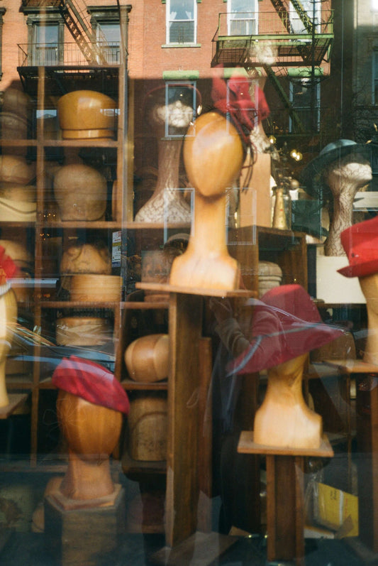 Display of wooden hat forms with red hats in a shop window, showcasing unique headwear styles, captured on Kodak ColorPlus 200 film.