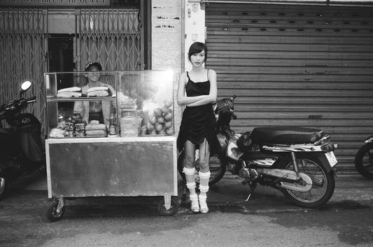 A young woman in a black dress stands beside a food cart on a street with motorcycles in black and white shot with Mr Negative Cash Only 100