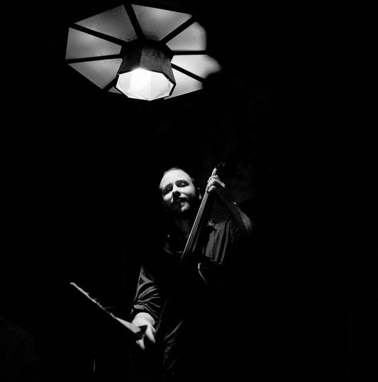Musician performing with double bass under a lamp in a dimly lit setting, captured on Ilford Delta 3200.