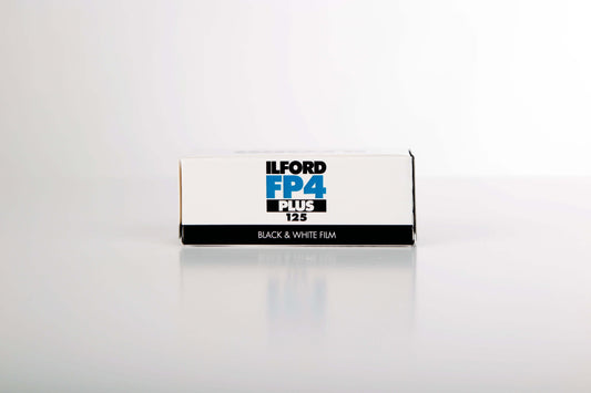 Ilford FP4 Plus 125 black and white film box on a reflective surface, ideal for ISO 125 photography.
