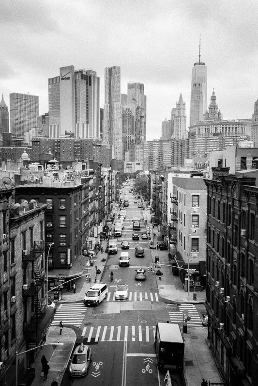 Black and white view of a busy New York City street with high rise buildings in the background.