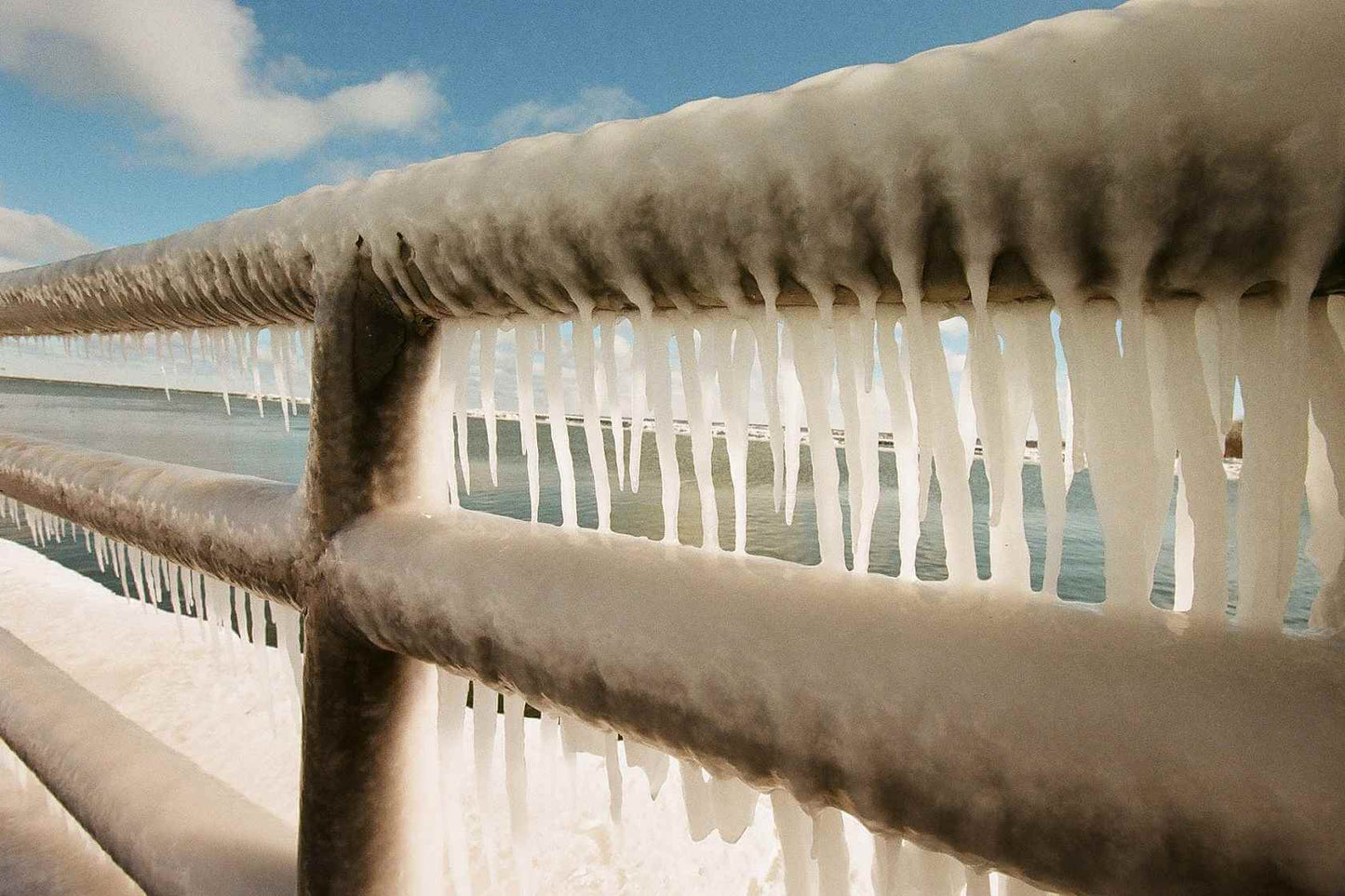Icicles hanging from a railing by the water, showcasing winter's beauty and frozen landscape, shot on Kodak Eastman Gold 200