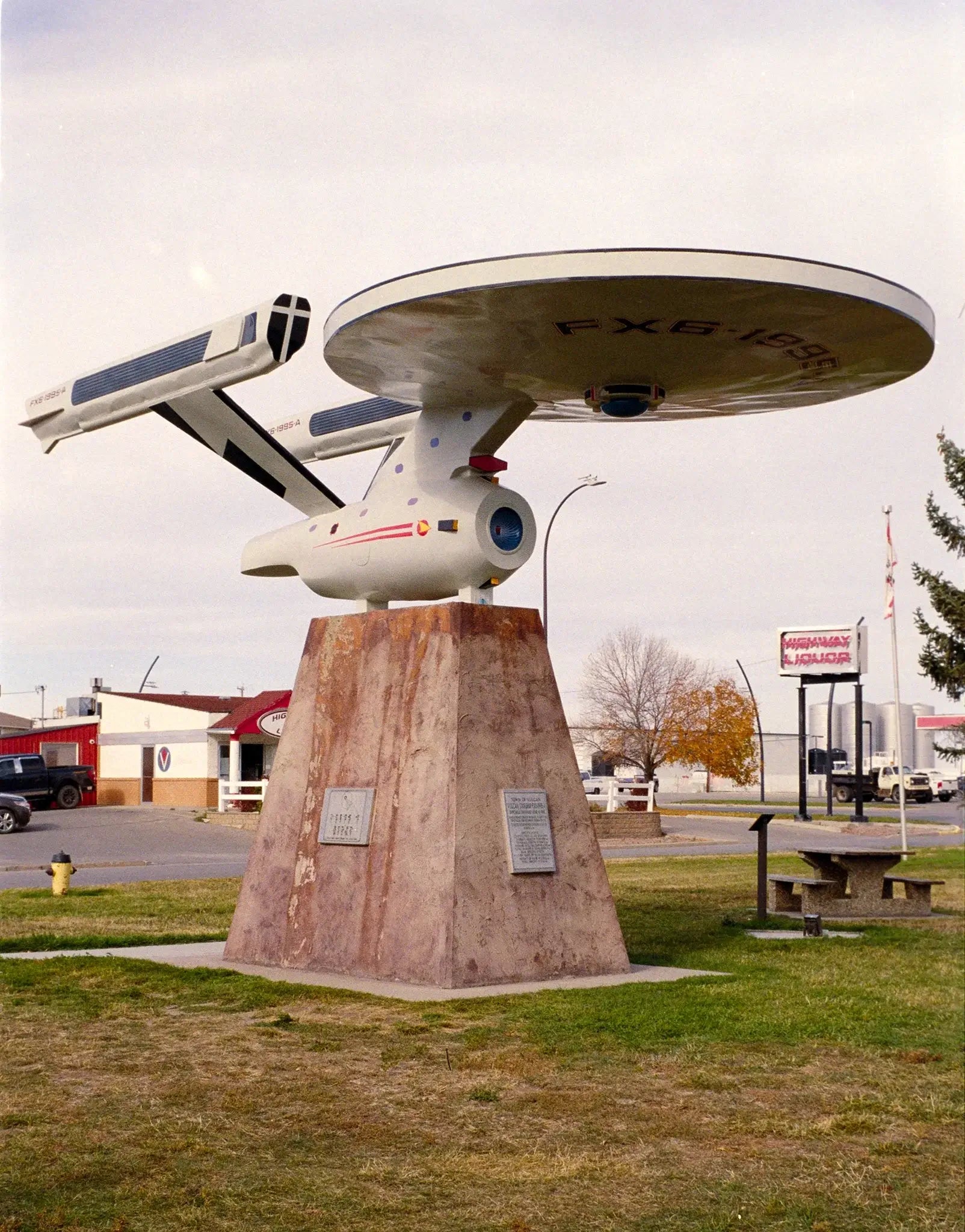 Street Candy Street Savvy Sample Image: Model of a spaceship sculpture on a pedestal in a park, showcasing a creative tribute to space exploration.