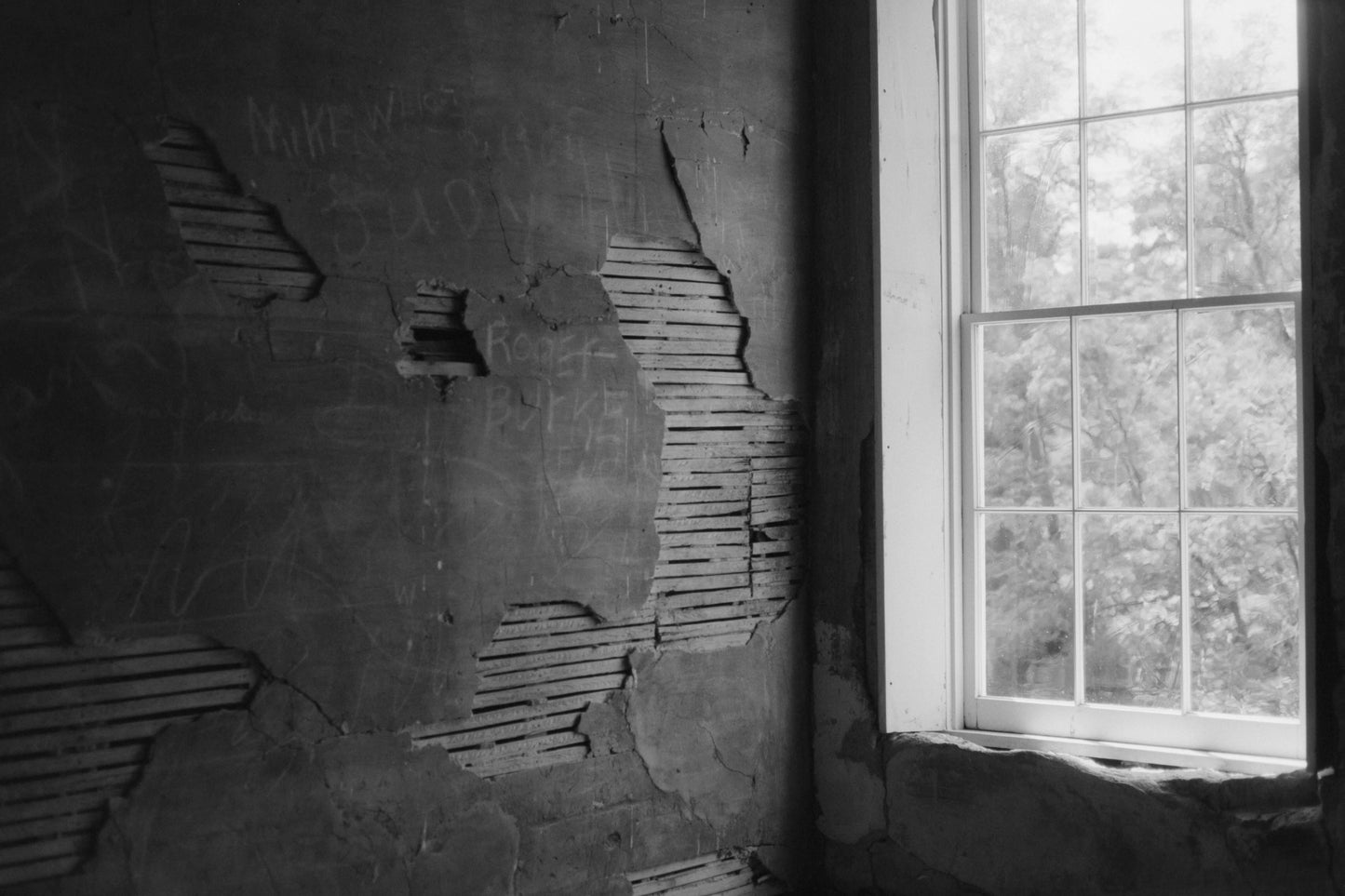 Black and white photograph of a weathered wall with peeling paint and a window letting in natural light shot with Mr Negative Cash Only 100