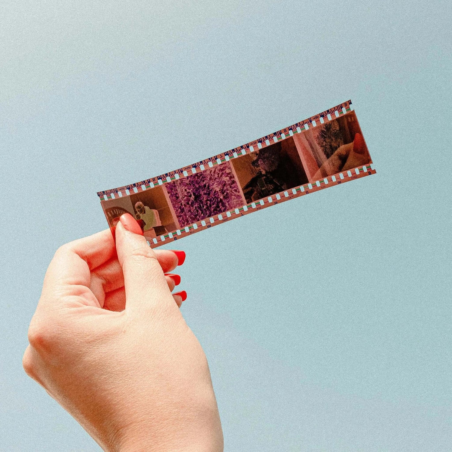 Hand holding with red nail polish holding strip of 35mm film against blue background.