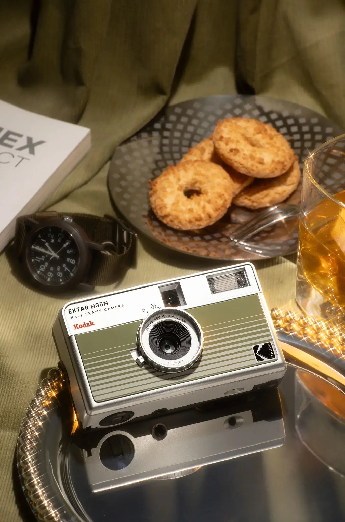 Kodak Ektar H35N Half Frame Film Camera (Green) displayed with cookies and a watch on a stylish table setting.