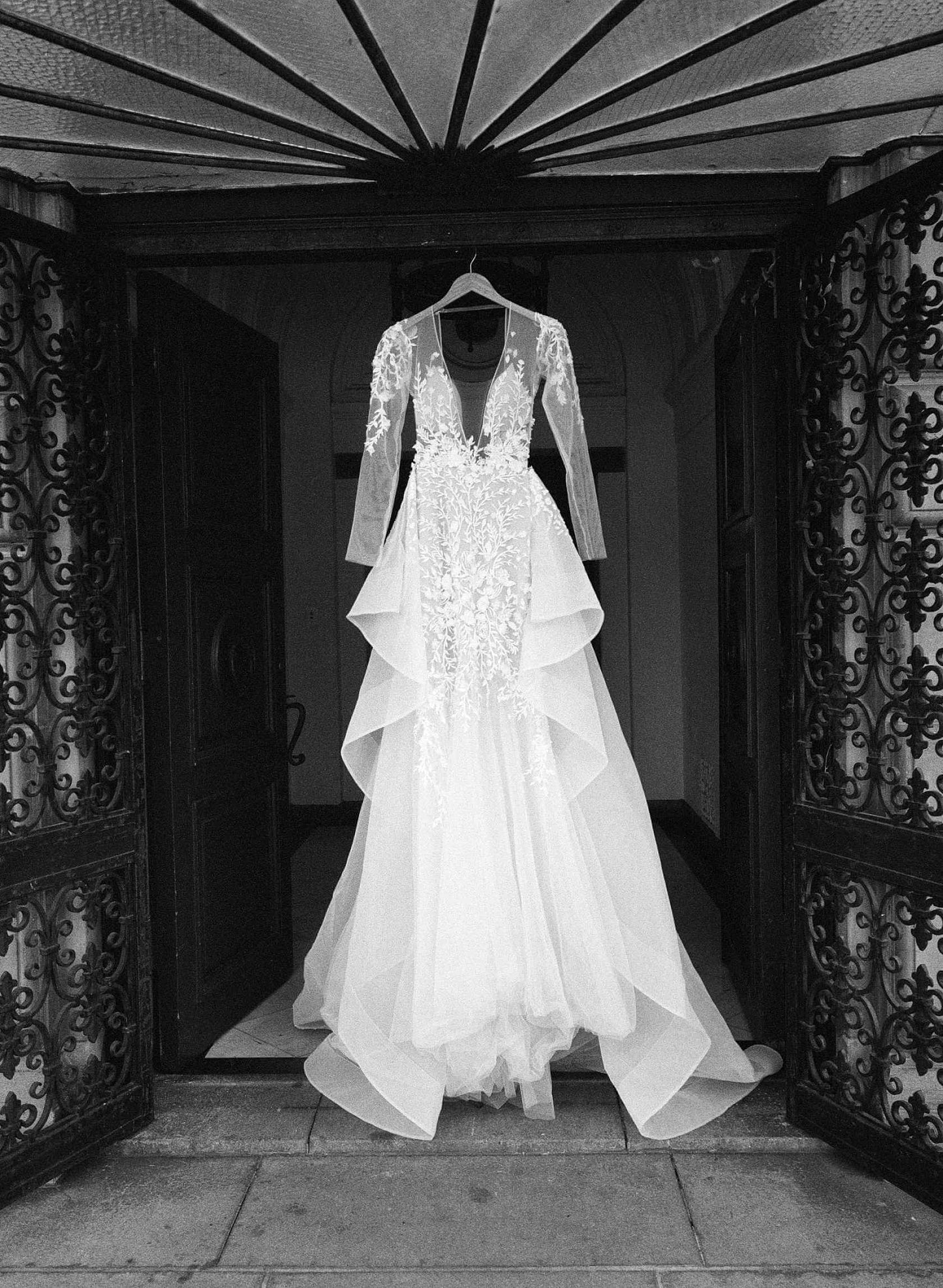 Elegant white wedding dress with lace details hanging at an ornate doorway, showcasing bridal fashion.
