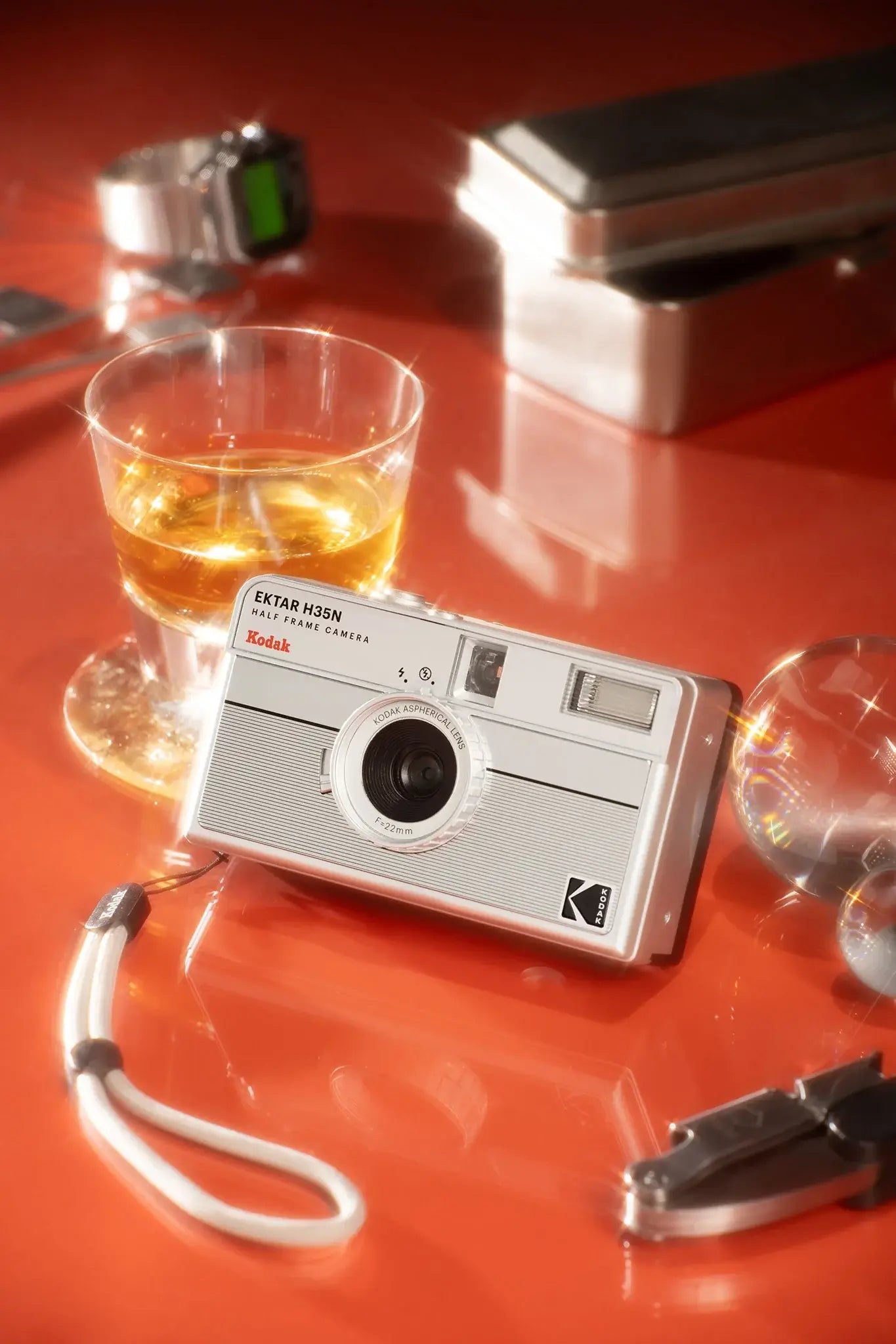 Kodak Ektar H35N Half Frame Film Camera (Striped Silver) on a table with a drink and accessories.