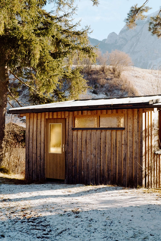 A wooden cabin with a glass door surrounded by trees and mountains, showcasing a serene winter landscape, shot on Kodak Eastman UltraMax 400