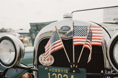 Close-up of a vintage Ford car hood adorned with American flags and license plate, shot on Psychedelic Street 400.