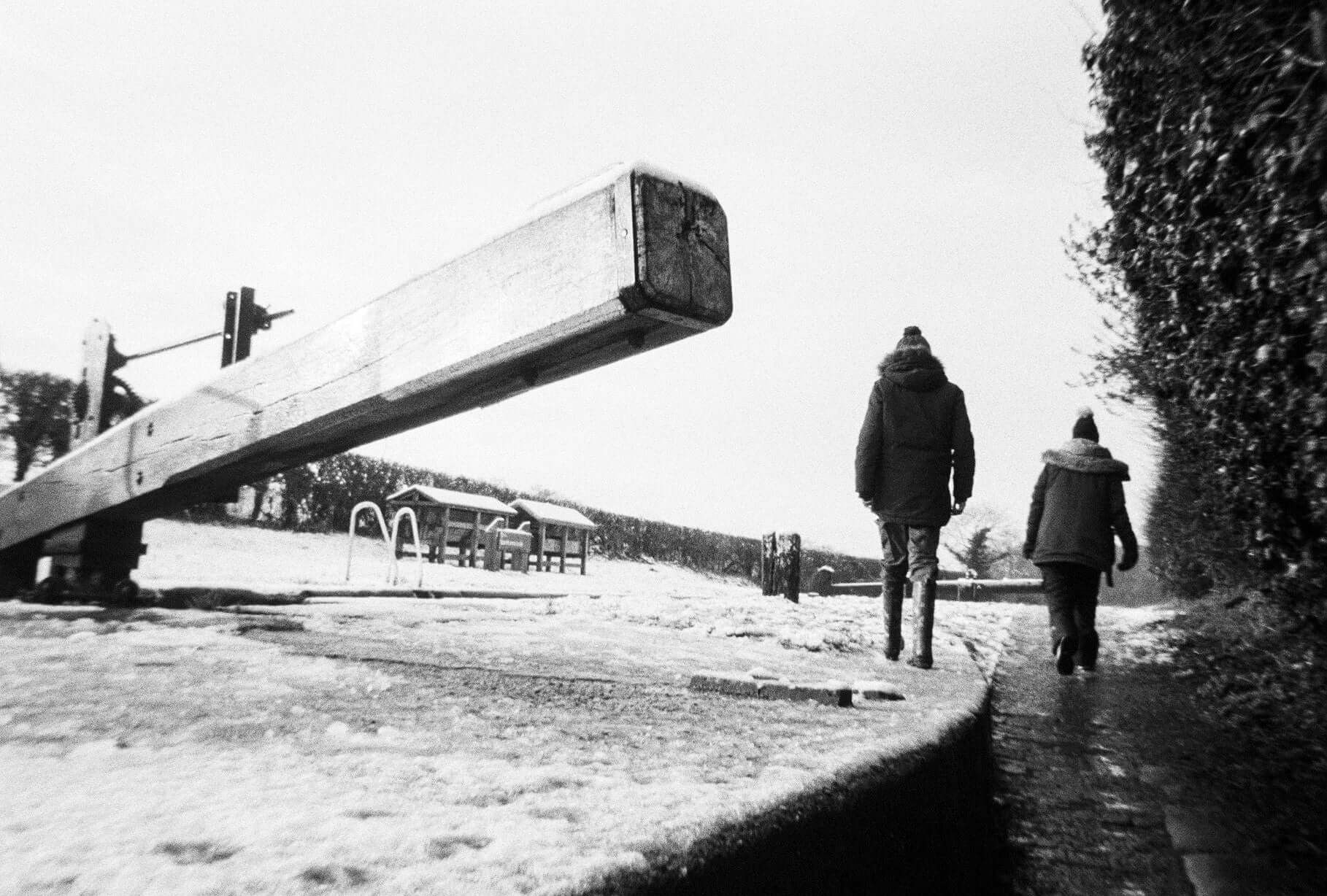 Harman EZ-35 Reusable 35mm Film Camera photo: a black-and-white scene of a person and child walking along a snowy path near a railway barrier, hinting at outdoor photography setup