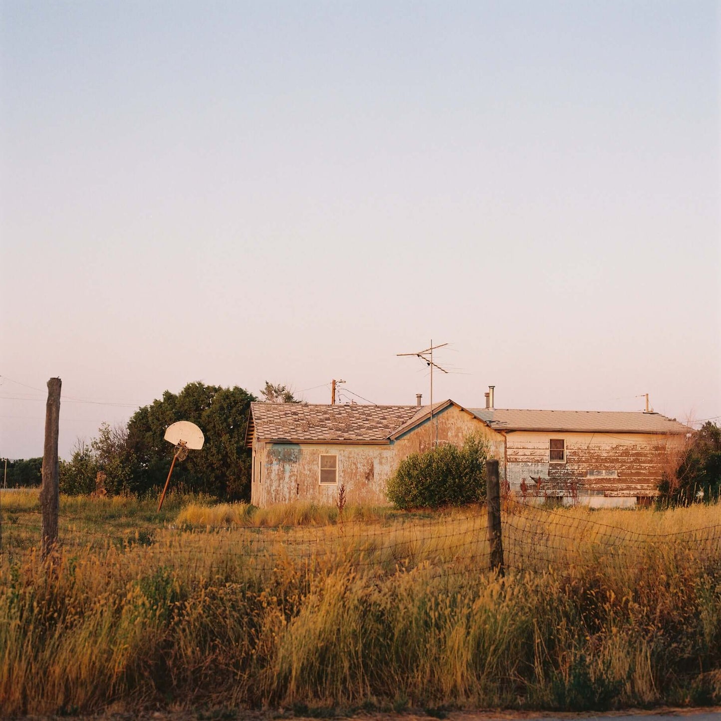 A weathered house with a satellite dish in a grassy field at sunset shot on Kodak Gold 200.