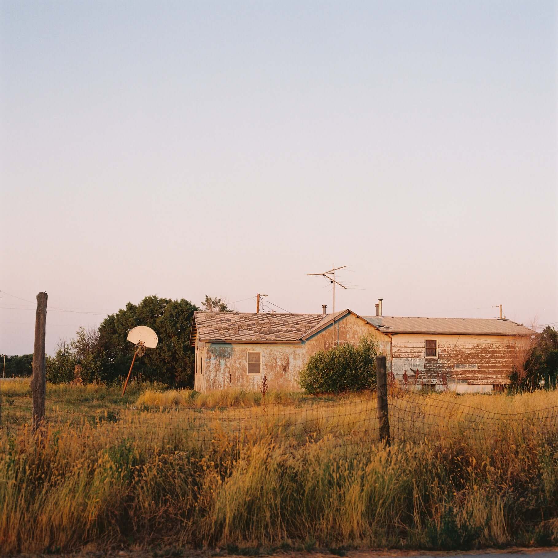 A weathered house with a satellite dish in a grassy field at sunset shot on Kodak Gold 200.