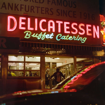 Neon sign of Delicatessen Buffet Catering at night with busy street scene and illuminated storefront. shot on Kodak Gold 200.