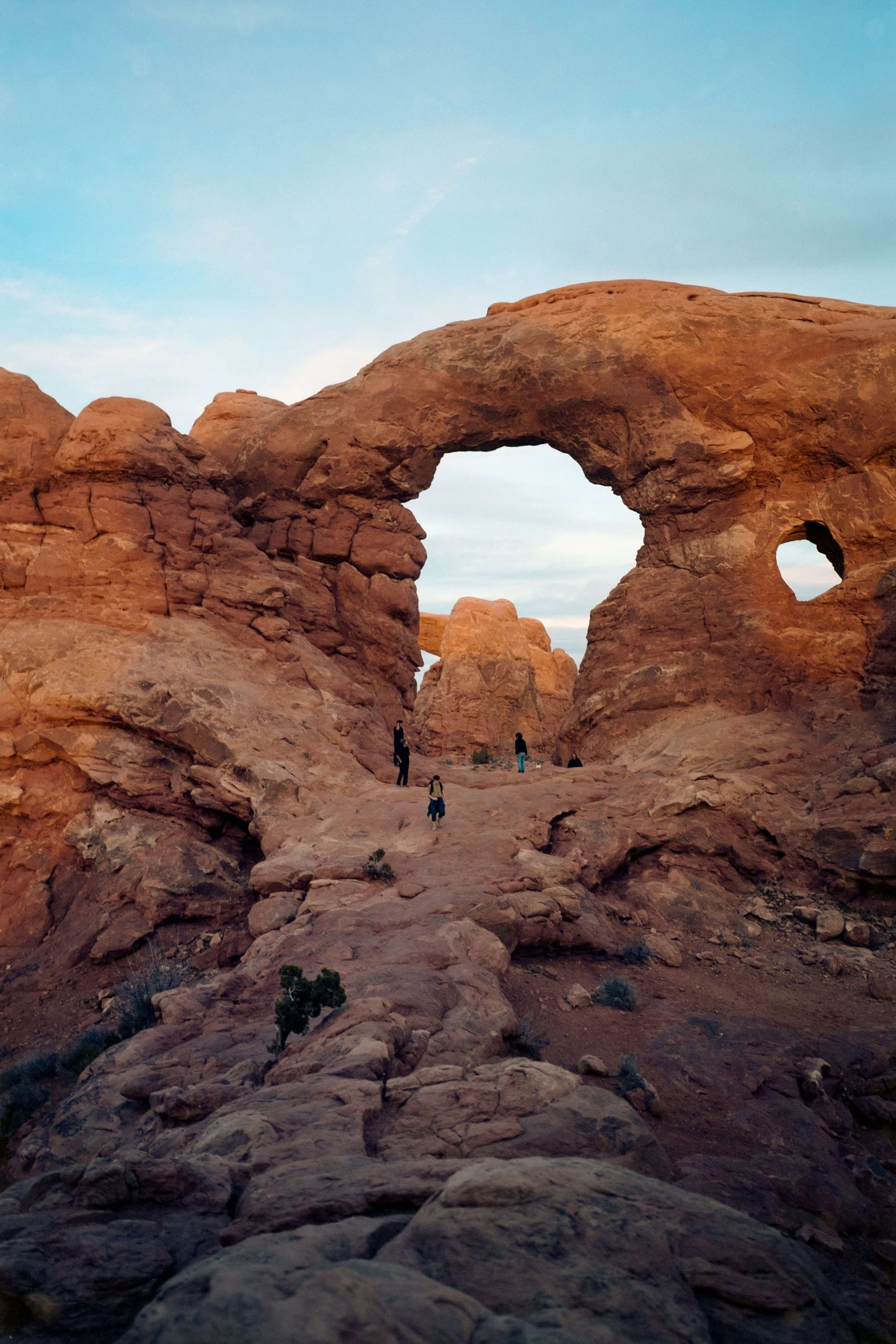 Scenic view of Arch Rock formation with hikers at Arches National Park, showcasing vibrant red rock landscape.