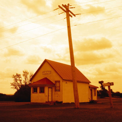 A vintage-style image of a small white house with a red roof and a power pole under an orange sky shot on Harman Red 125