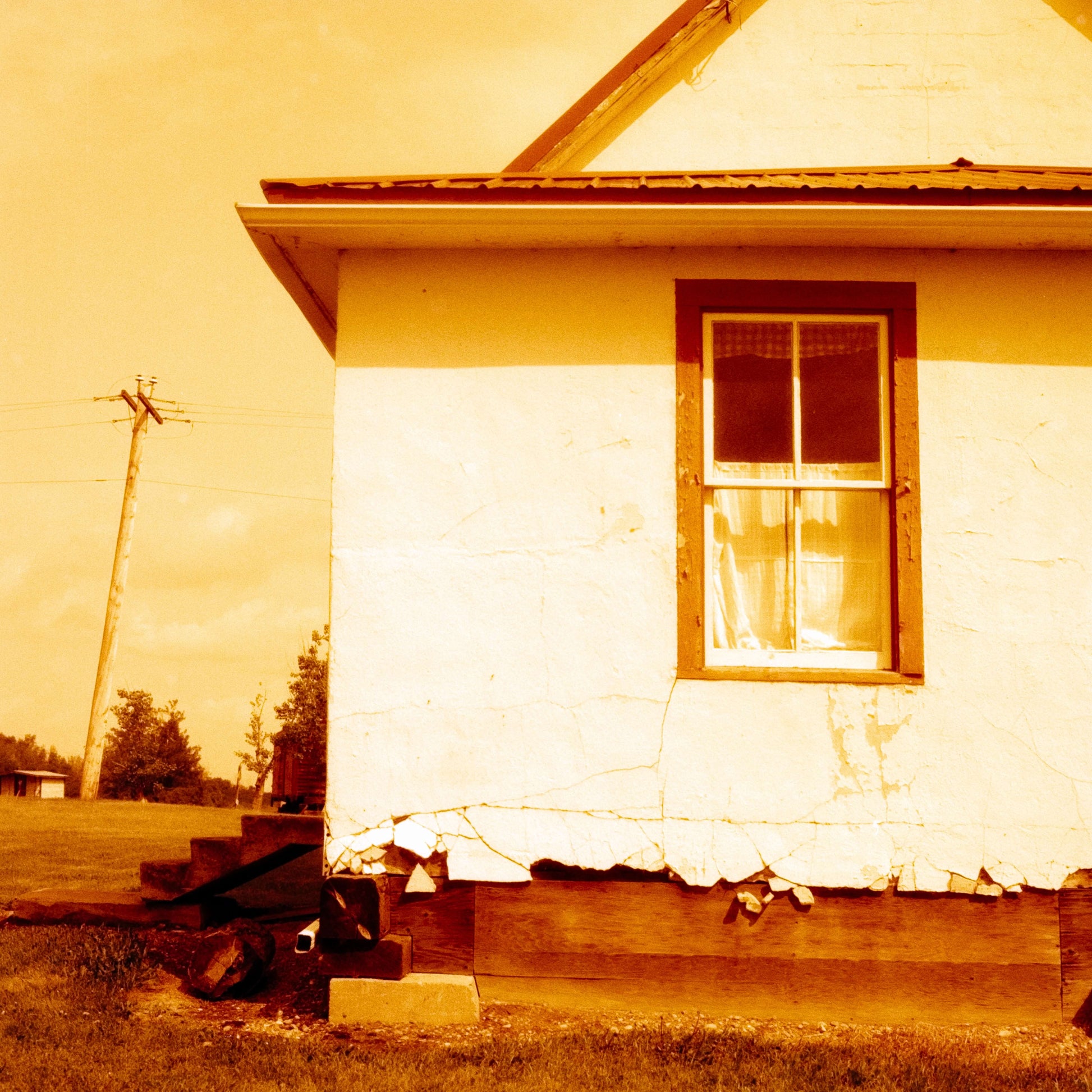 A close-up of an old house exterior with cracked paint, an orange hue, and a single window, showcasing a weathered rural setting, shot on Harman Red 125