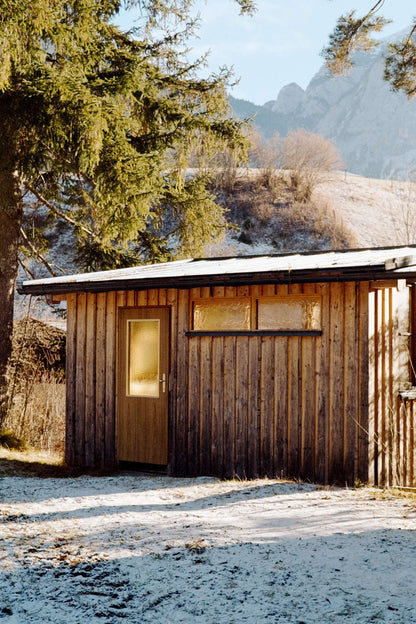 A wooden cabin with a glass door surrounded by trees and mountains, showcasing a serene winter landscape, shot on Kodak Eastman UltraMax 400