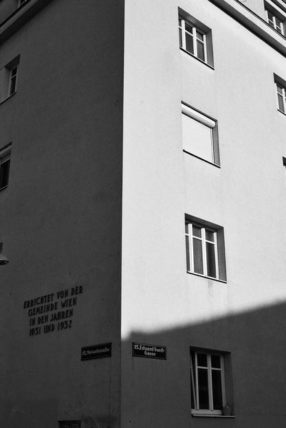 Black and white photograph of a building corner with street signs and shadows.