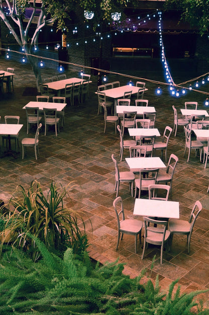 Outdoor seating area with tables and chairs surrounded by greenery and string lights at night shot with Harman Switch Azure 125