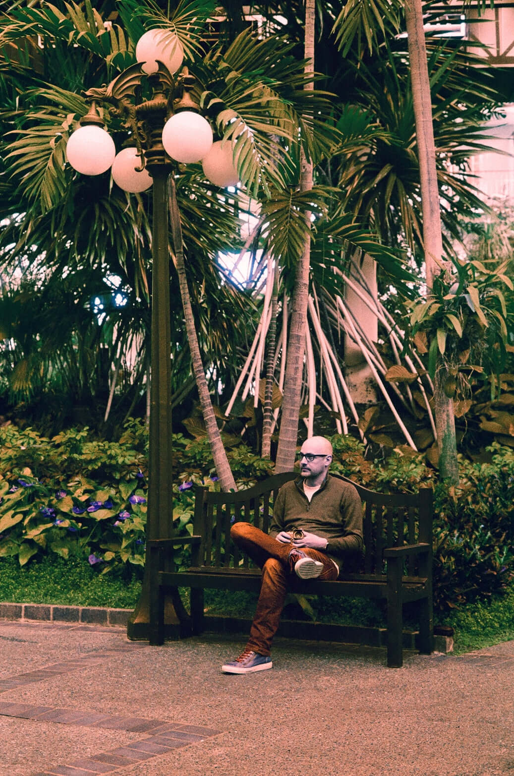 Harman Switch Azure 125 color negative film photograph of a man sitting on a bench in a lush garden.