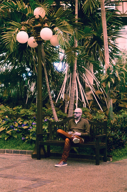 Harman Switch Azure 125 color negative film photograph of a man sitting on a bench in a lush garden.