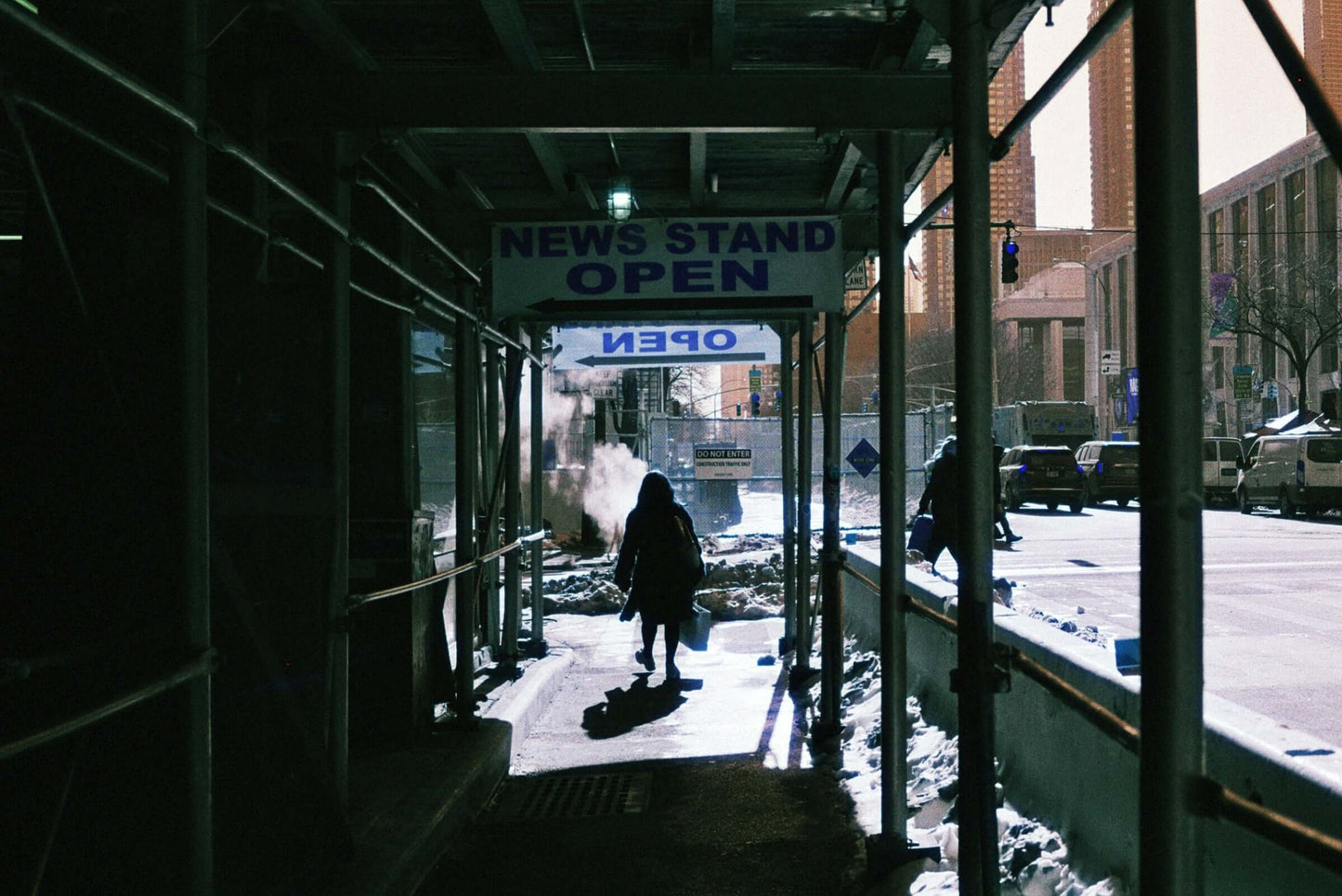 Harman Switch Azure 125 color negative film showcasing person walking past an open newsstand under scaffolding in an urban setting.