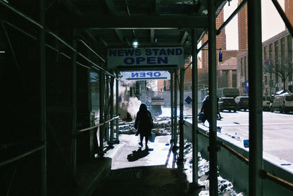 Harman Switch Azure 125 color negative film showcasing person walking past an open newsstand under scaffolding in an urban setting.
