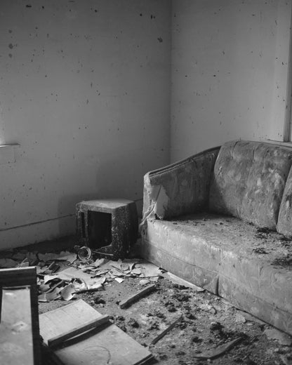 abandoned room with a worn couch, debris, and decayed surroundings in black and white photography.