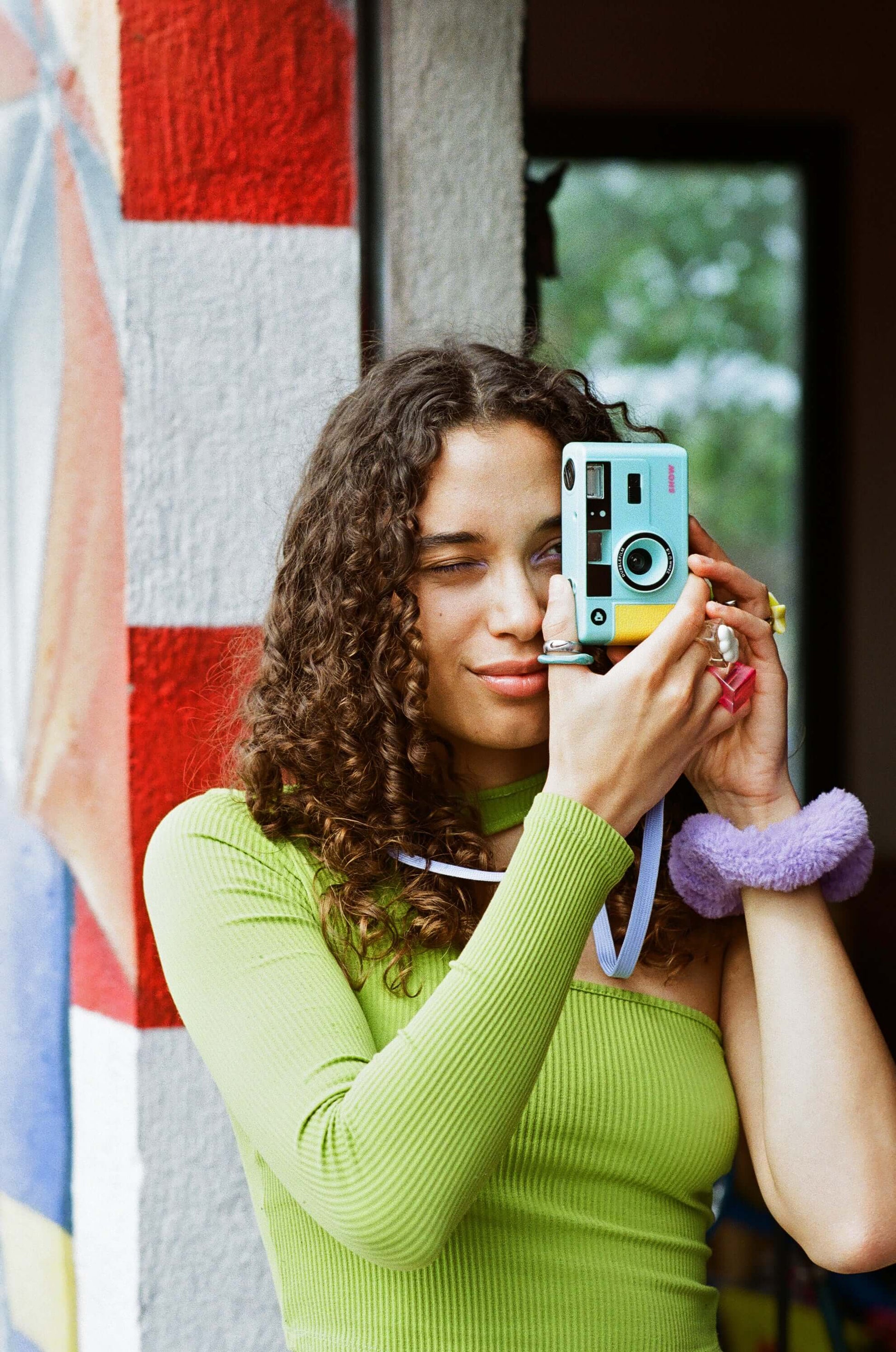 Dubblefilm SHOW 35mm Reusable Camera (Turquoise) in turquoise held by woman taking a photo, showcasing built-in flash and casual carry strap setup