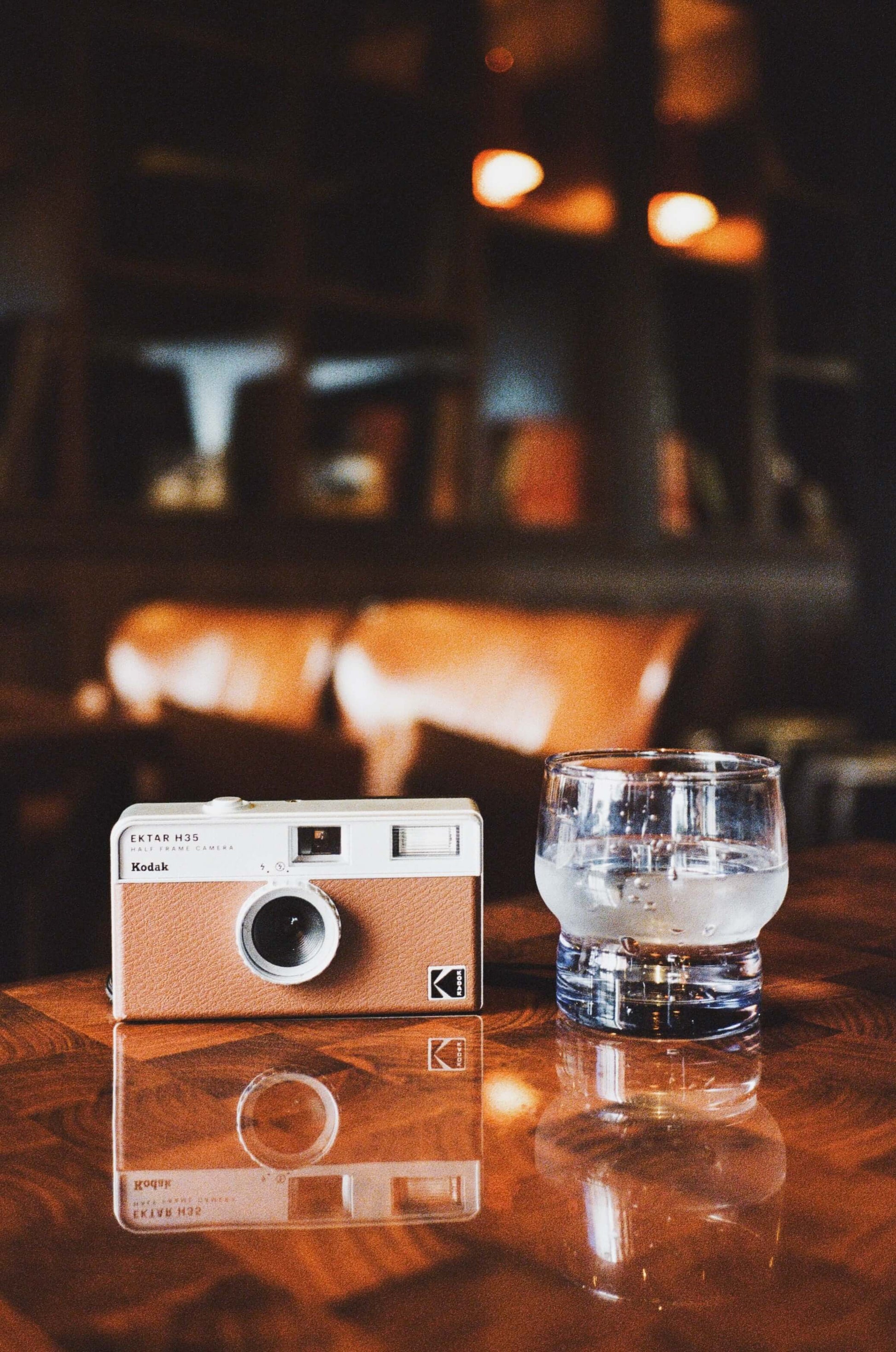 Kodak Ektar H35 Half Frame Film Camera (Brown) next to a glass of water on a wooden table.