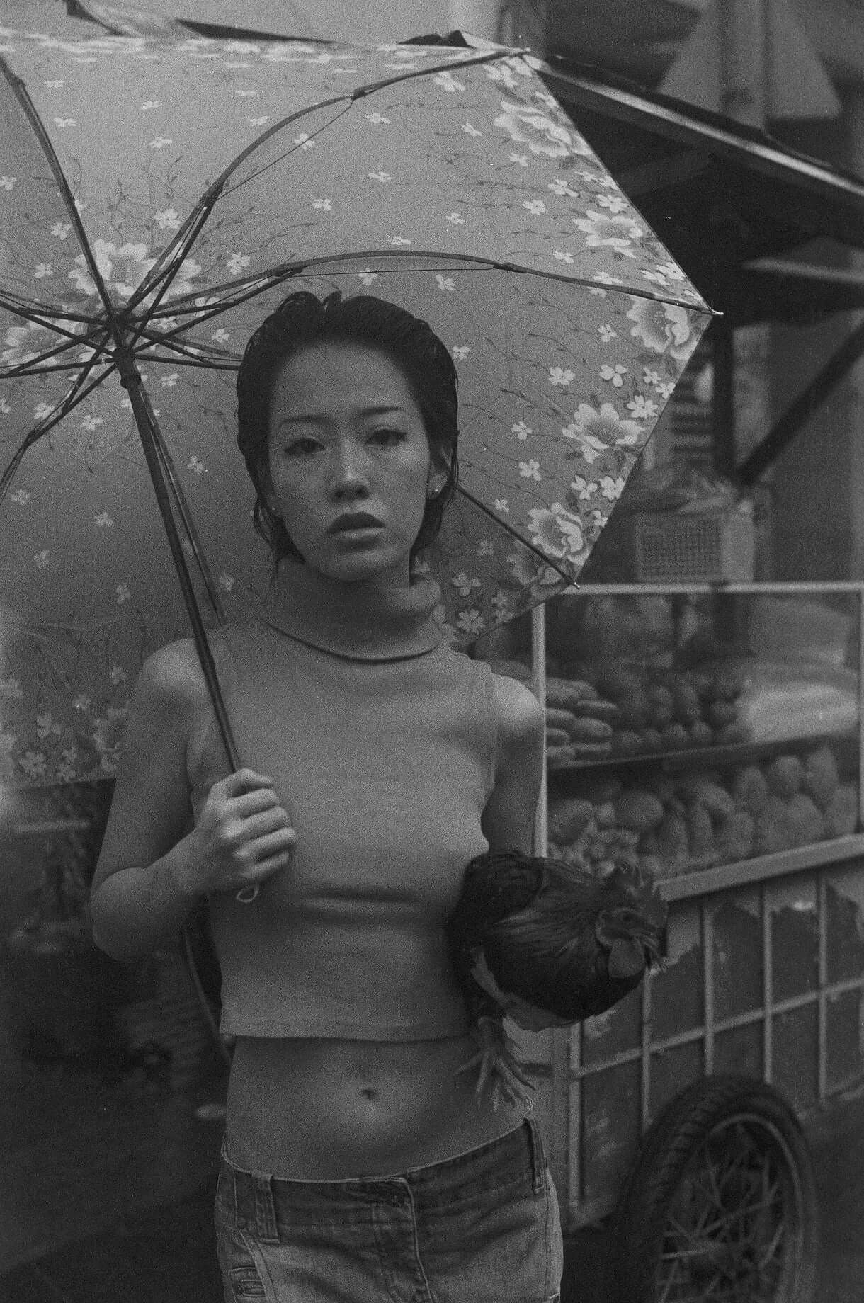 A woman holding a chicken under a floral umbrella in a black and white street scene shot on Mr Negative Black Market 250