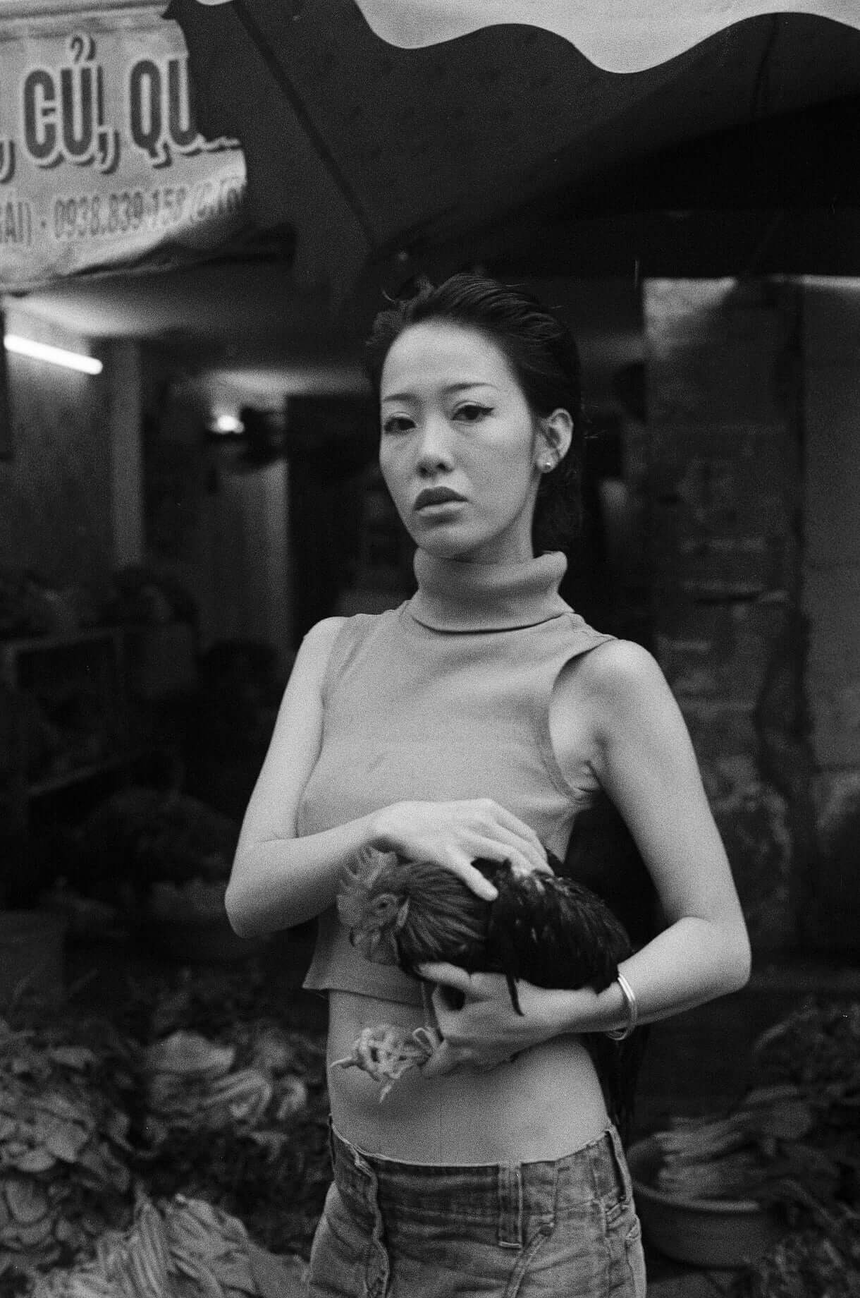 Young woman in a sleeveless top holding a chicken in a market, shot on Mr Negative Black Market 250