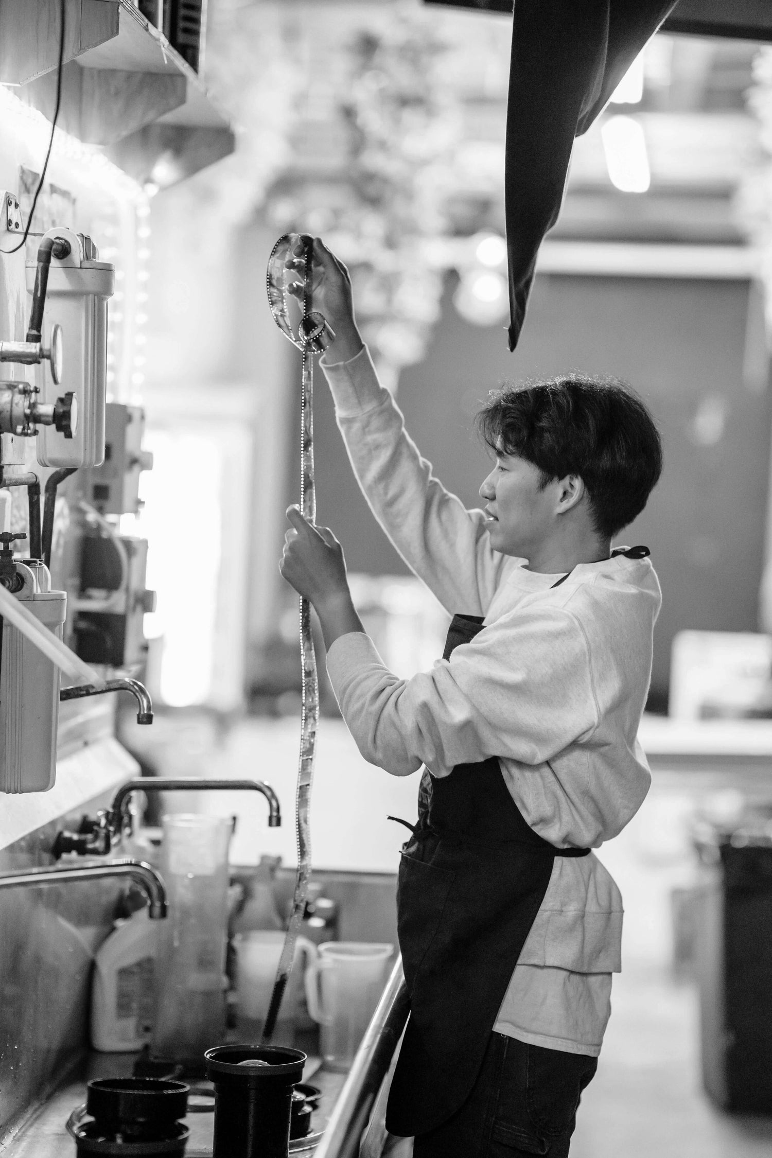 A person develops black and white film, holding a film strip above a sink in a photography lab.
