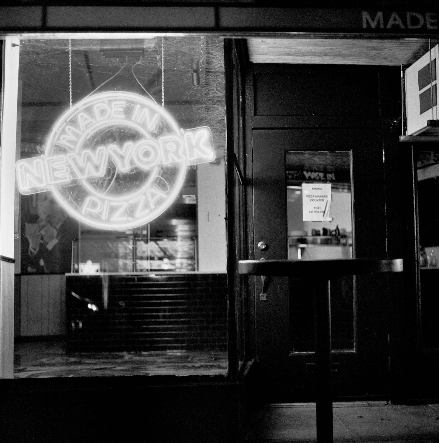 Neon sign reading 'Made in New York Pizza' illuminated at night in a restaurant window, captured on Ilford Delta 3200.