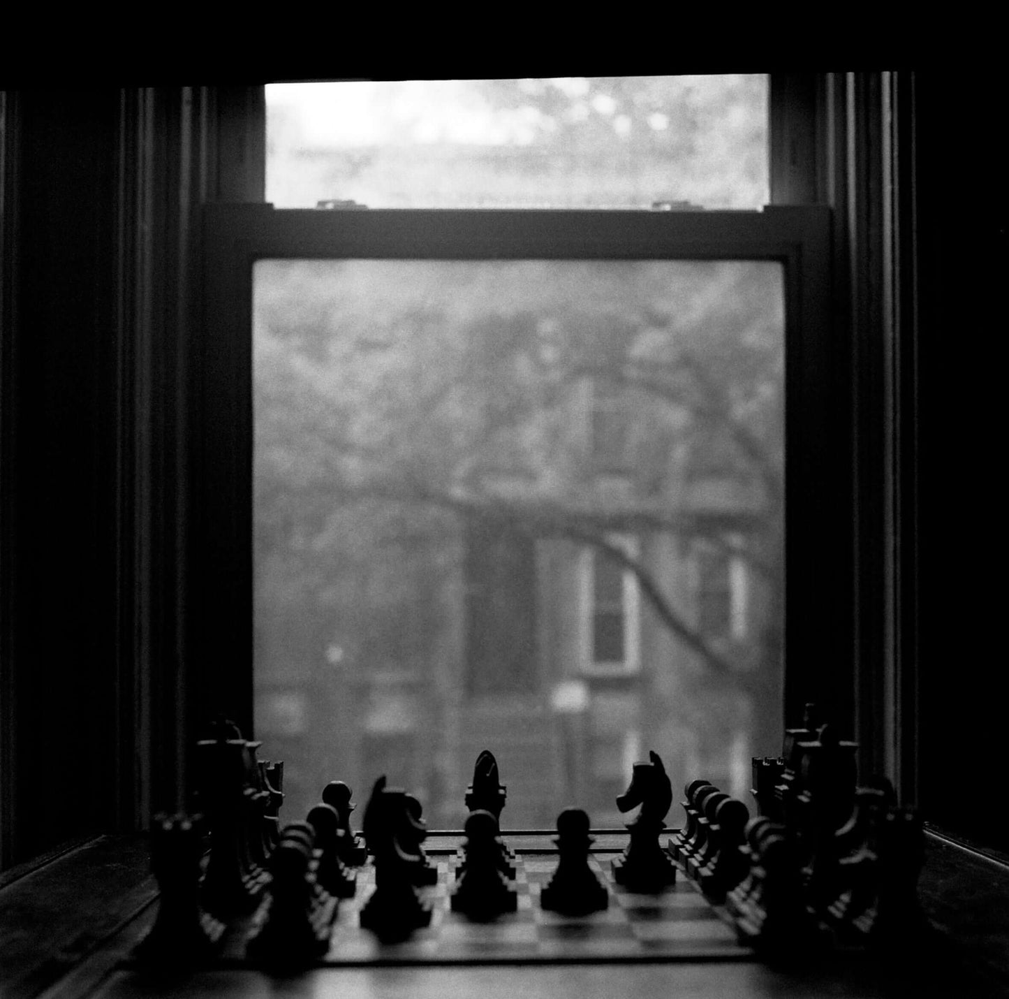 Black and white photograph of a chessboard in front of a window, creating a moody atmosphere, captured on Ilford Delta 3200.