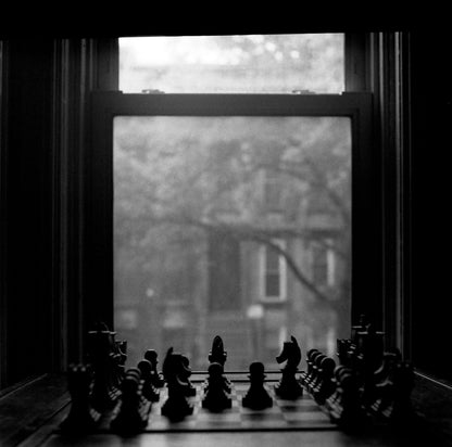 Black and white photograph of a chessboard in front of a window, creating a moody atmosphere, captured on Ilford Delta 3200.