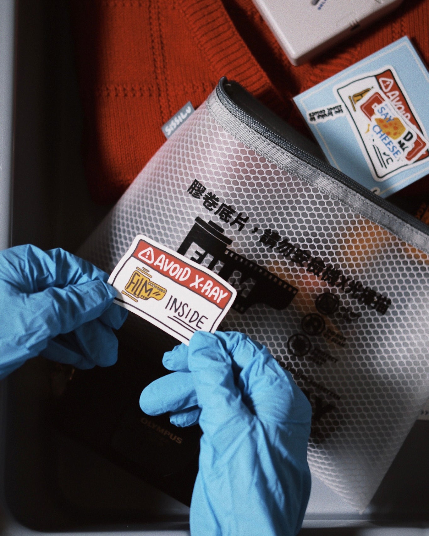 Hands with blue gloves placing a warning sticker on the SissiLu "DO NOT X‑RAY" Film Pouch.