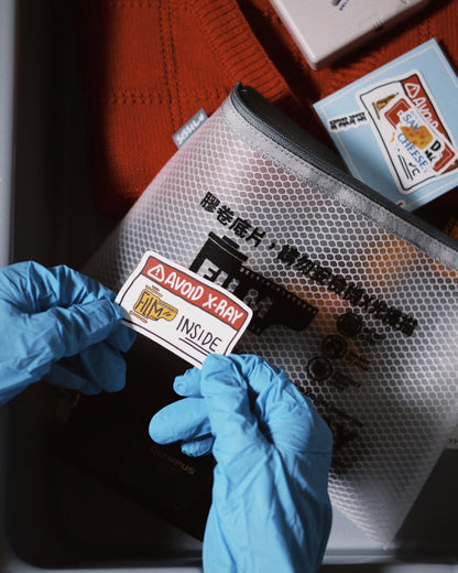 Hands with blue gloves placing a warning sticker on the SissiLu "DO NOT X‑RAY" Film Pouch.