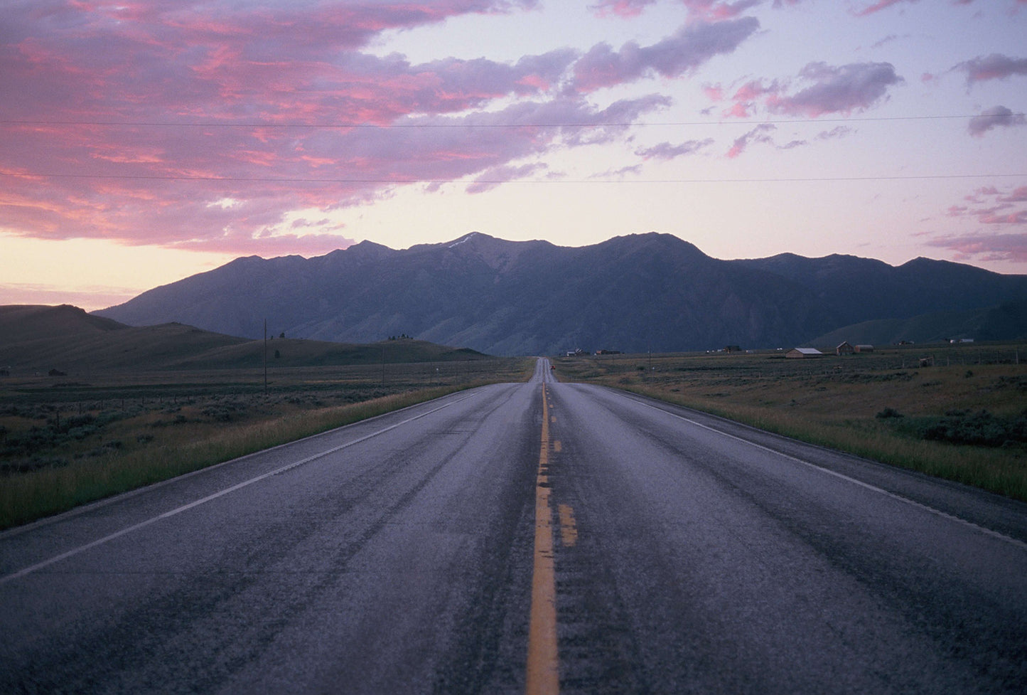 Scenic view of a long road leading to mountains under a colorful sunset sky.