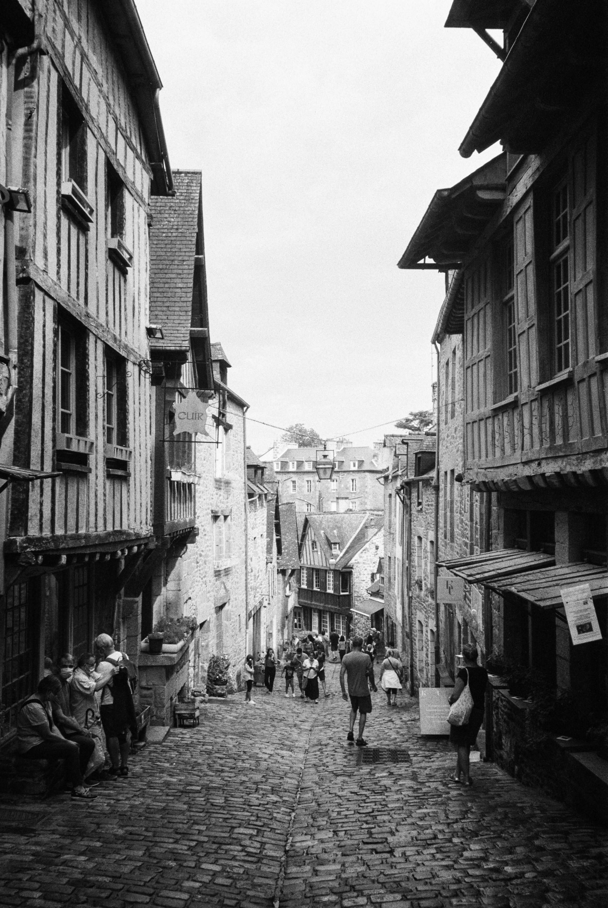 Historic cobblestone street with timber-framed buildings, people walking in black and white photography, shot with Ilford HP5 Plus B&W Single-Use Film Camera