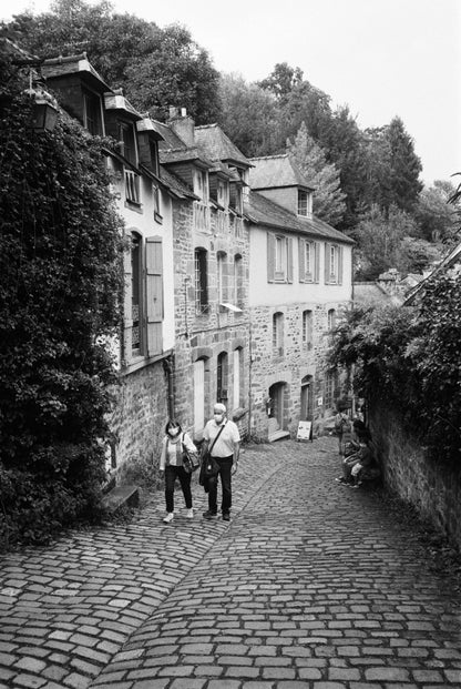 Couple walking down a cobblestone street lined with historic buildings in a black and white photography style, shot with Ilford HP5 Plus B&W Single-Use Film Camera