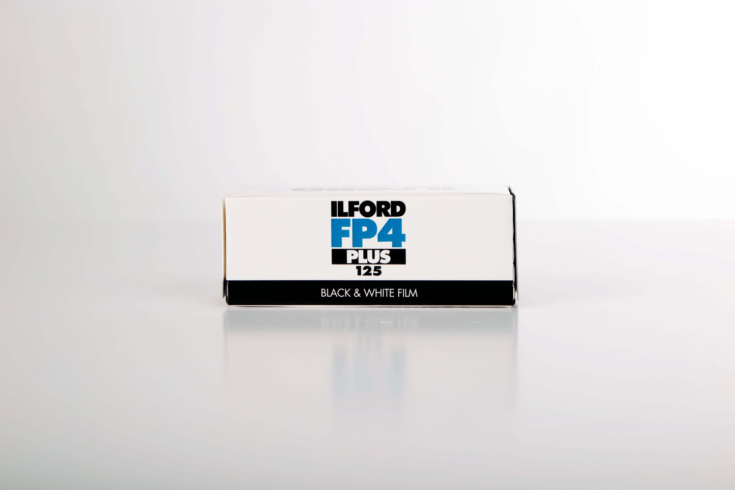 Ilford FP4 Plus 125 black and white film box on a reflective surface, ideal for ISO 125 photography.