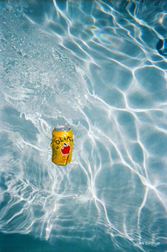 Yellow soda can floating in clear blue pool water reflecting sunlight on surface shot with Kodak EC35.