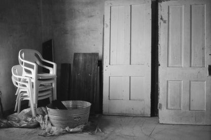 Black and white photograph of stacked plastic chairs and wooden doors in an indoor space, capturing a vintage feel shot with Mr Negative Cash Only 100