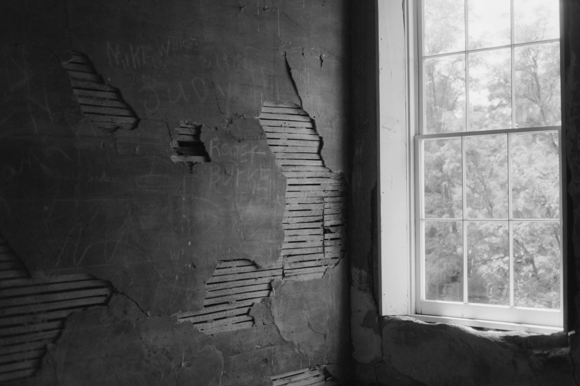 Black and white photograph of a weathered wall with peeling paint and a window letting in natural light shot with Mr Negative Cash Only 100