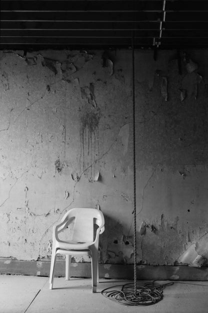 A solitary plastic chair in front of an aged, textured wall with a rope hanging nearby, captured in black and white shot with Mr Negative Cash Only 100
