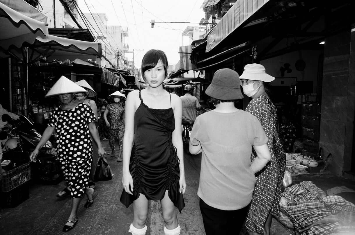 Model standing in a bustling market surrounded by shoppers, captured in striking black and white shot with Mr Negative Cash Only 100