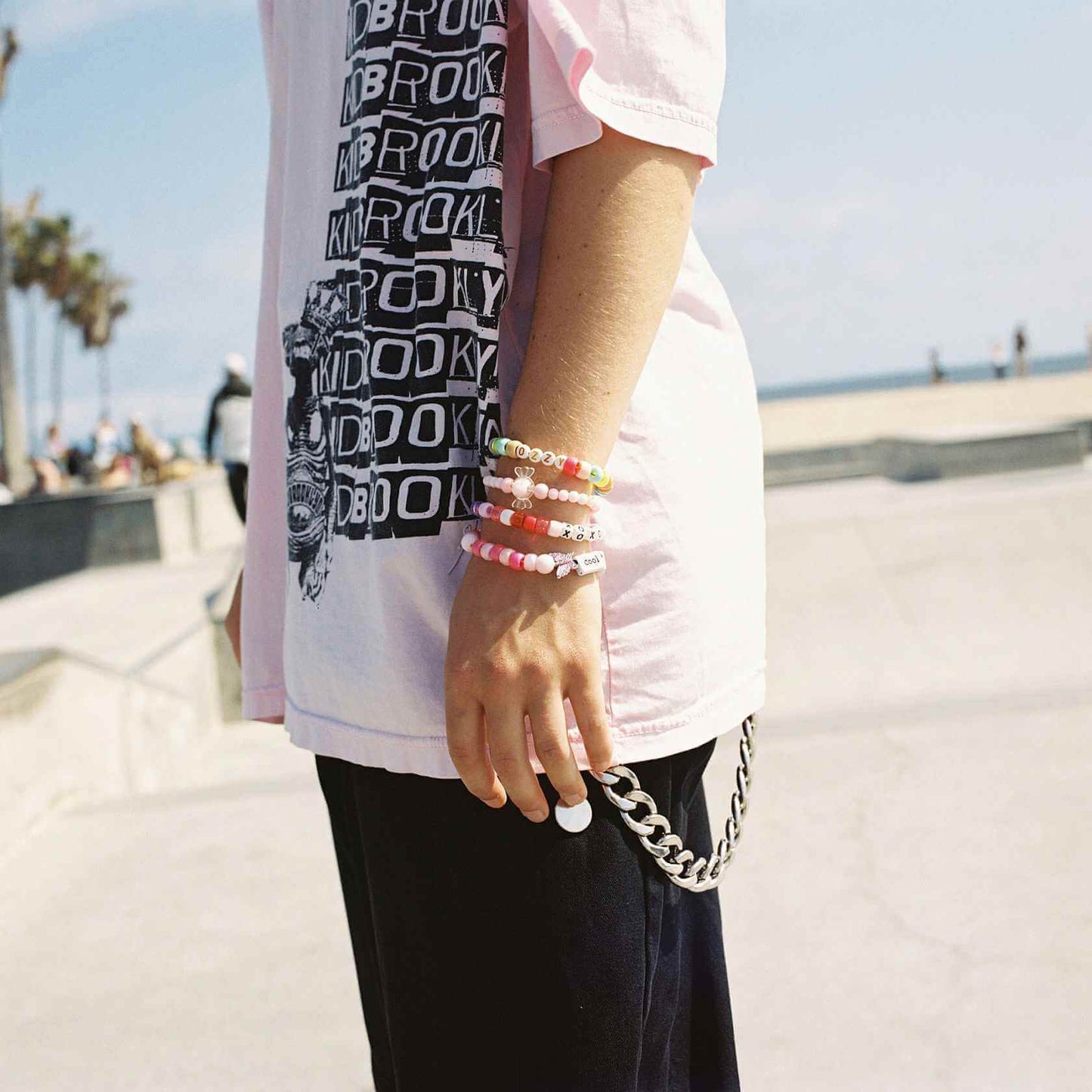 Person wearing a pink shirt with a graphic and colorful bead bracelets by the beach.