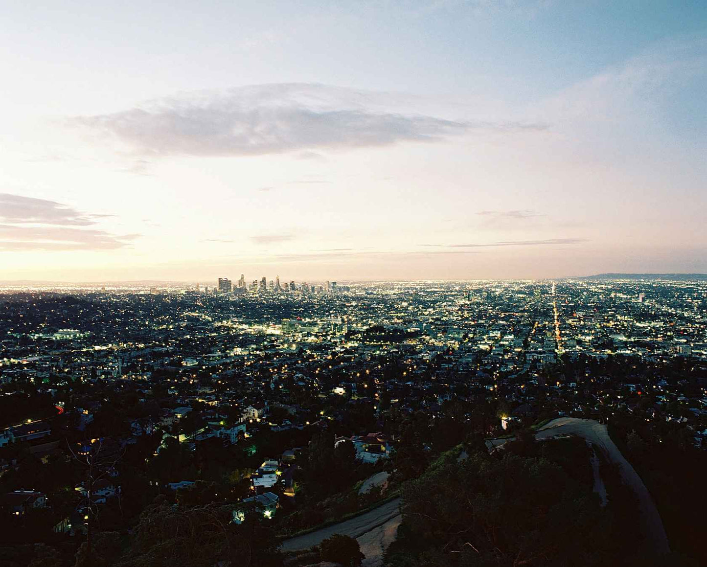 A stunning aerial view of a vibrant city skyline at dusk, showcasing twinkling lights and a soft evening sky.